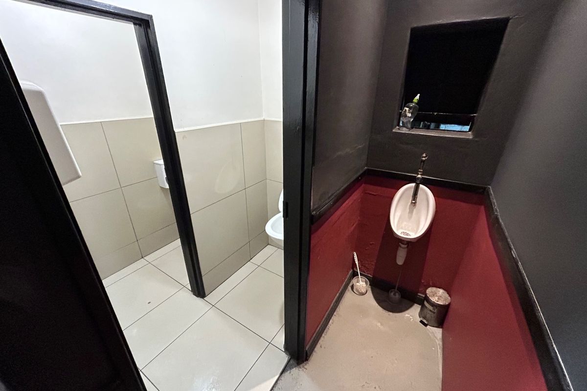 A functional commercial restroom facility featuring a wall-mounted urinal in a dedicated alcove and a separate partitioned toilet cubicle with tiled flooring.