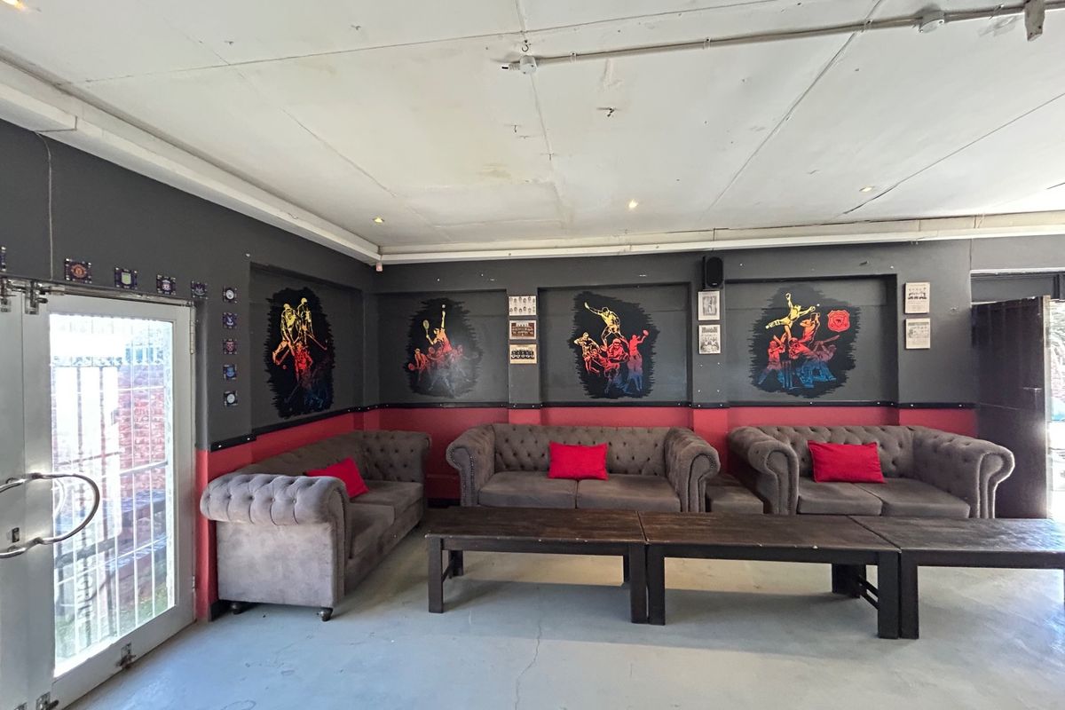 A spacious lounge area featuring dark grey walls with decorative murals, tiled flooring, and double glass door access.