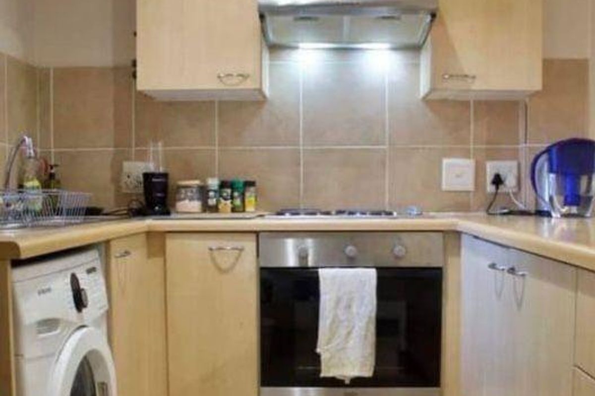 Compact kitchen featuring light wood cabinetry, built-in oven, extractor fan, and integrated laundry space with tiled backsplash and countertop.