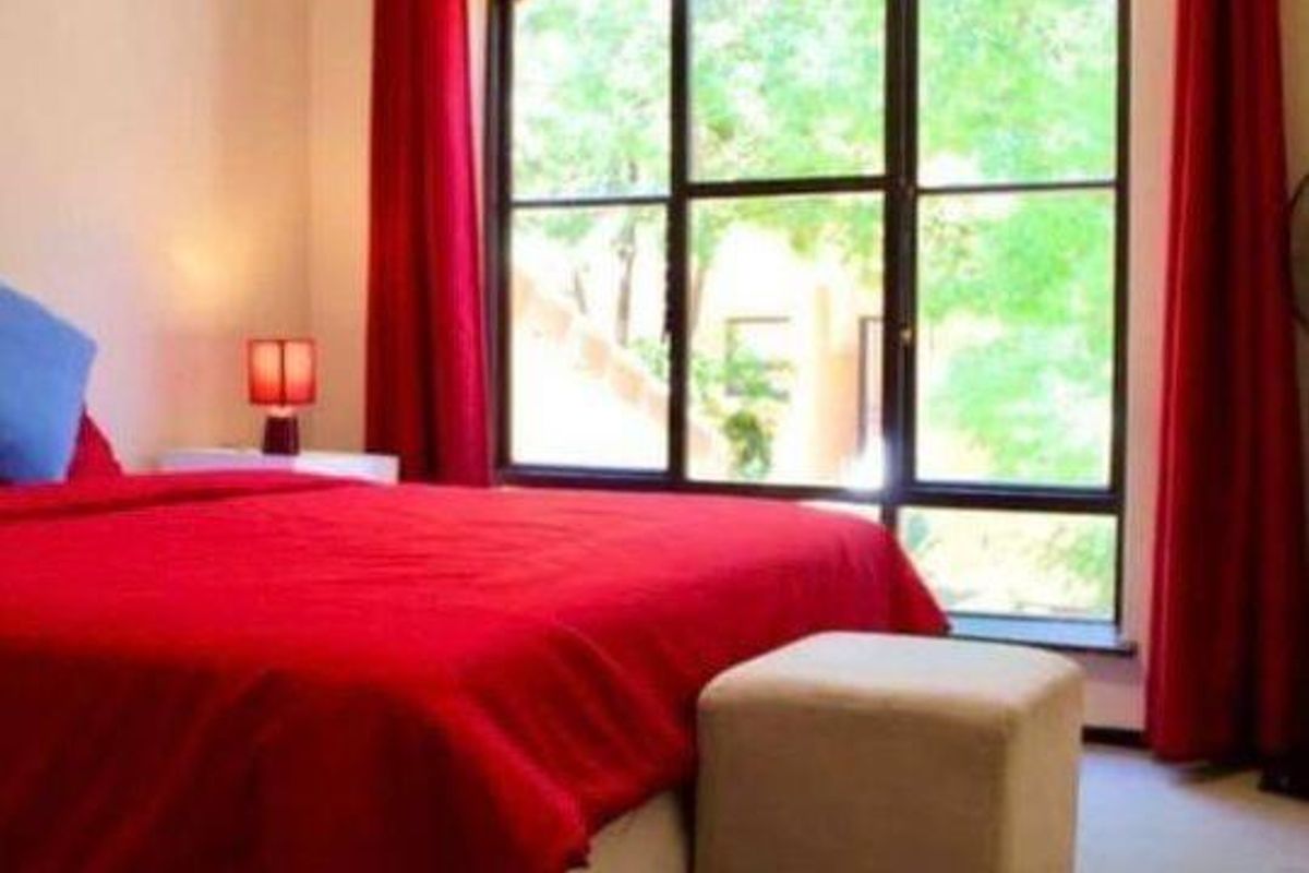 A bedroom featuring a large arched window with dark frames, providing natural light and a view of the surrounding greenery.