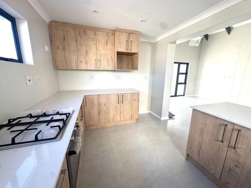 Modern kitchen featuring light wood-look cabinetry, stone countertops, a gas hob, and built-in oven, with neutral tiled flooring and an open-plan layout.