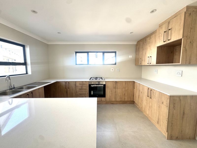 Modern kitchen featuring light wood-grain cabinetry, stone countertops, integrated gas hob, built-in oven, and neutral tiled flooring in a clean, open layout.