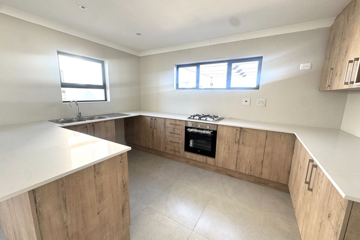 Modern kitchen featuring light wood-grain cabinetry, stone countertops, built-in oven, gas hob, and neutral tiled flooring in a clean, contemporary layout.