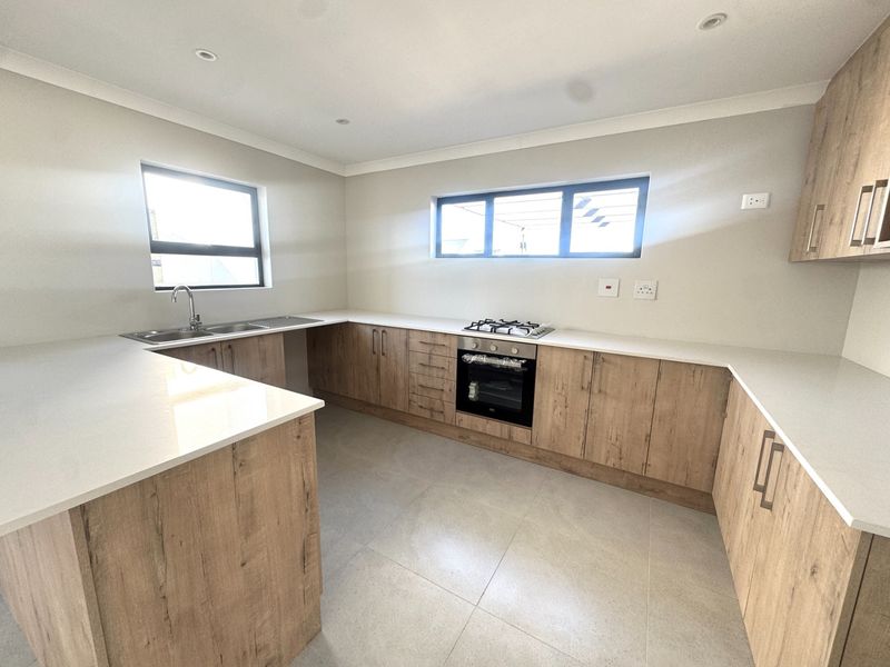 Modern kitchen featuring light wood-grain cabinetry, stone countertops, built-in oven, gas hob, and neutral tiled flooring in a clean, contemporary layout.