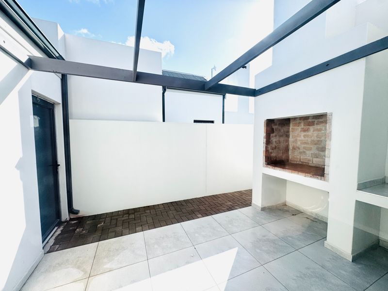 Outdoor patio area featuring a built-in brick braai, overhead pergola structure, and a combination of tiled and paved flooring.