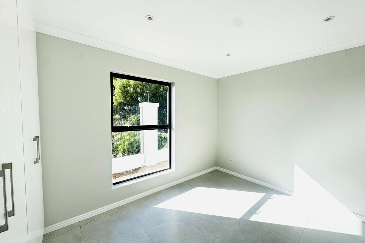 A bright, modern, and empty bedroom featuring neutral tiled flooring, built-in cupboards, and recessed downlighting.
