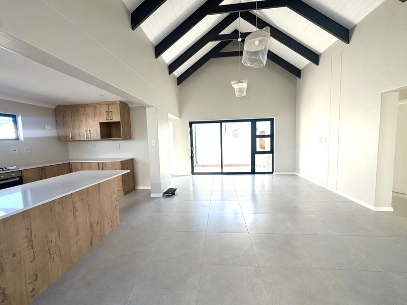 Spacious open-plan living and kitchen area featuring a high vaulted ceiling with exposed beams, modern cabinetry, and large sliding doors leading outdoors.