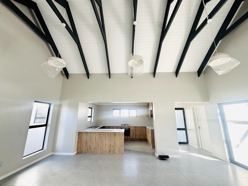 Spacious open-plan living and kitchen area featuring high vaulted ceilings with exposed beams, modern cabinetry, and neutral tiled flooring throughout.