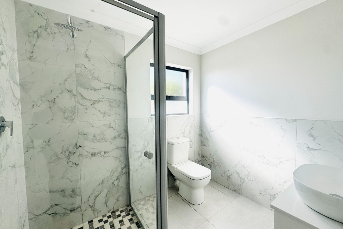 Modern bathroom featuring a walk-in shower with rainfall head, marble-look wall tiling, mosaic shower floor, and a contemporary vessel sink.
