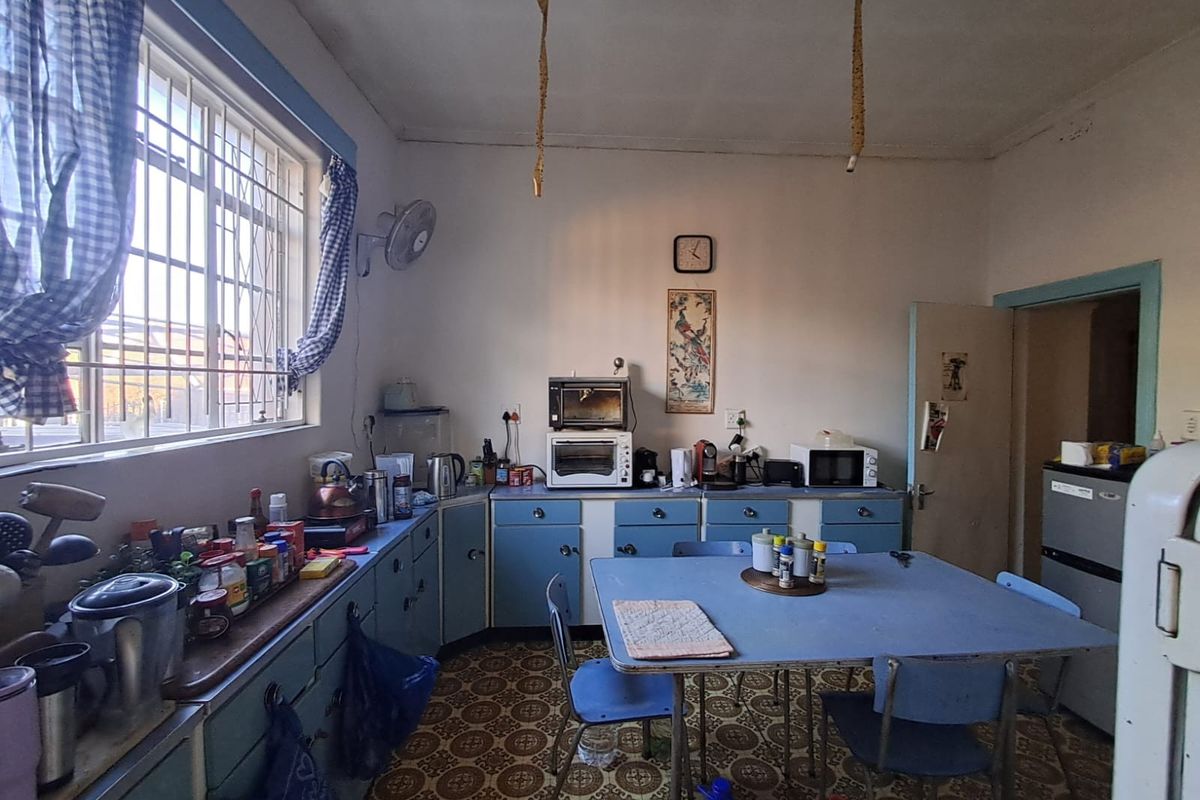 A dated kitchen featuring original blue cabinetry, patterned vinyl flooring, and a large window with security bars, offering a functional but aged space.