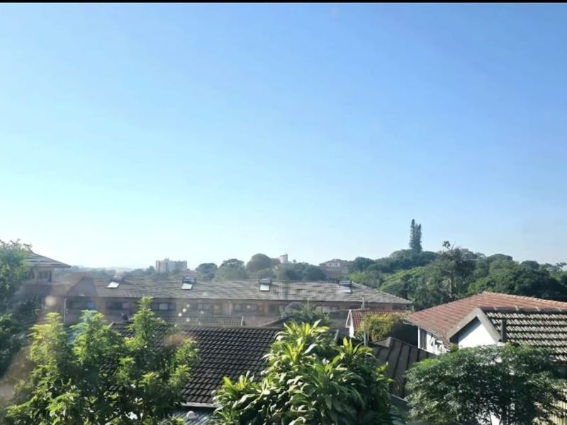 An elevated view overlooking the surrounding neighbourhood rooftops and lush green trees under a clear blue sky.