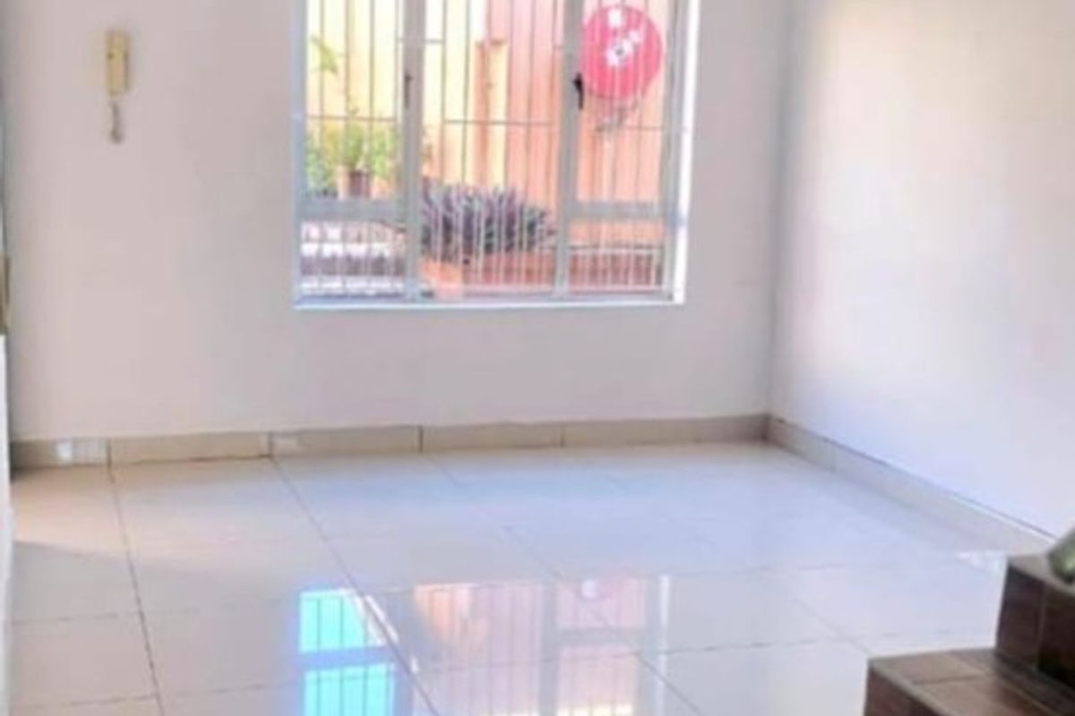 An open-plan living area featuring polished floor tiles, a staircase with wood-look treads, and a window fitted with security bars.