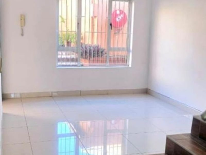 An open-plan living area featuring polished floor tiles, a staircase with wood-look treads, and a window fitted with security bars.