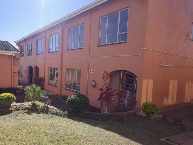 Exterior view of a multi-story townhouse complex featuring a communal garden, paved walkways, and secure gated entrances with aluminium window frames.