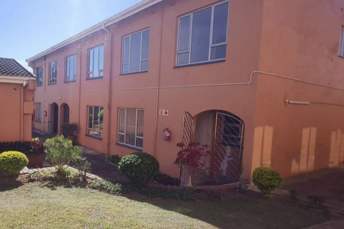 Exterior view of a multi-story townhouse complex featuring a communal garden, paved walkways, and secure gated entrances with aluminium window frames.