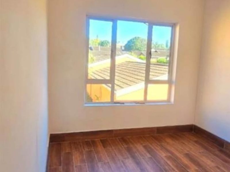 A bright, empty bedroom featuring wood-look tile flooring, neutral walls, and a large window providing natural light.