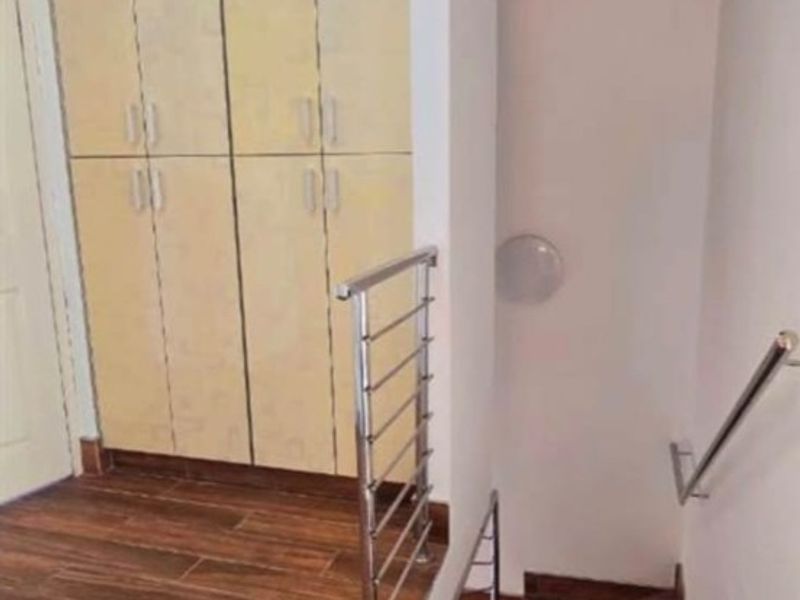 A staircase landing area featuring wood-look tile flooring, built-in storage cabinetry, and a modern stainless steel balustrade.