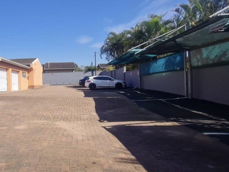 A paved parking area featuring covered carports and garage access within a townhouse complex.