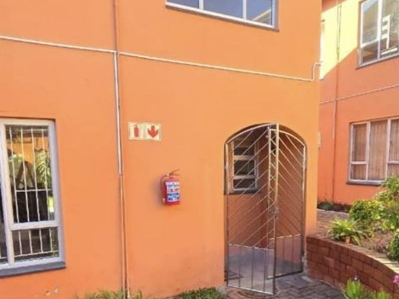 Exterior view of a townhouse featuring a paved courtyard, security gate, and fire safety equipment mounted on the orange-toned facade.
