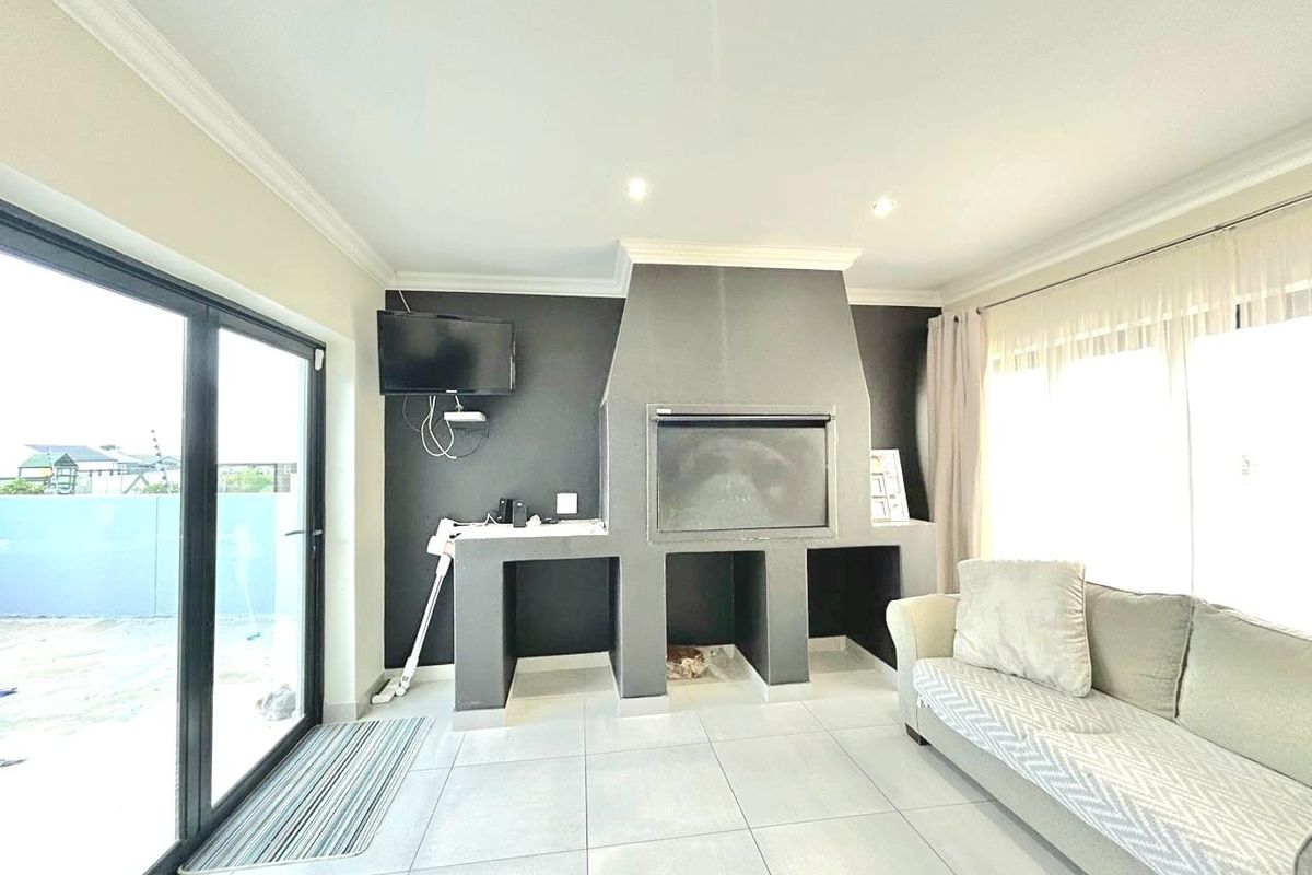 Living area featuring a built-in indoor braai fireplace, tiled flooring, and large sliding glass doors providing access to the outdoor space.