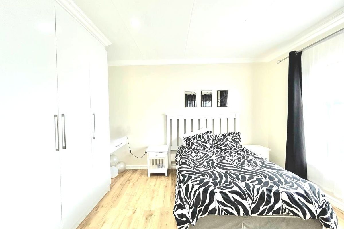 A bright bedroom featuring light wood-look flooring, built-in white cabinetry, and a neutral color palette.