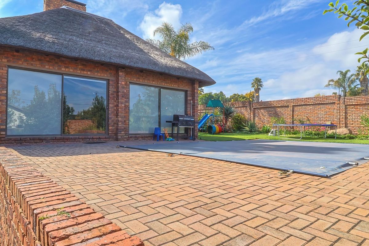Spacious backyard featuring a paved patio area, a swimming pool with a safety cover, and a brick-built structure with a traditional thatch roof.