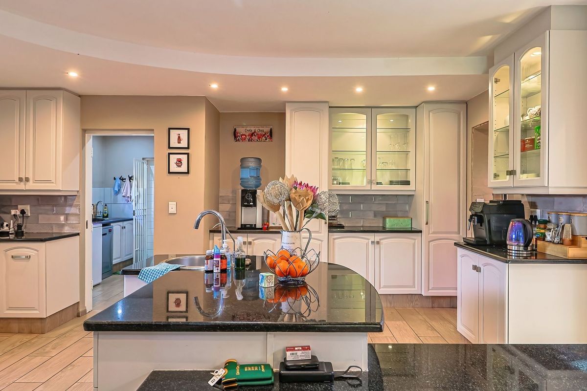 A well-appointed kitchen featuring granite countertops, custom cabinetry with glass-front display units, recessed lighting, and a central island with an integrated sink.