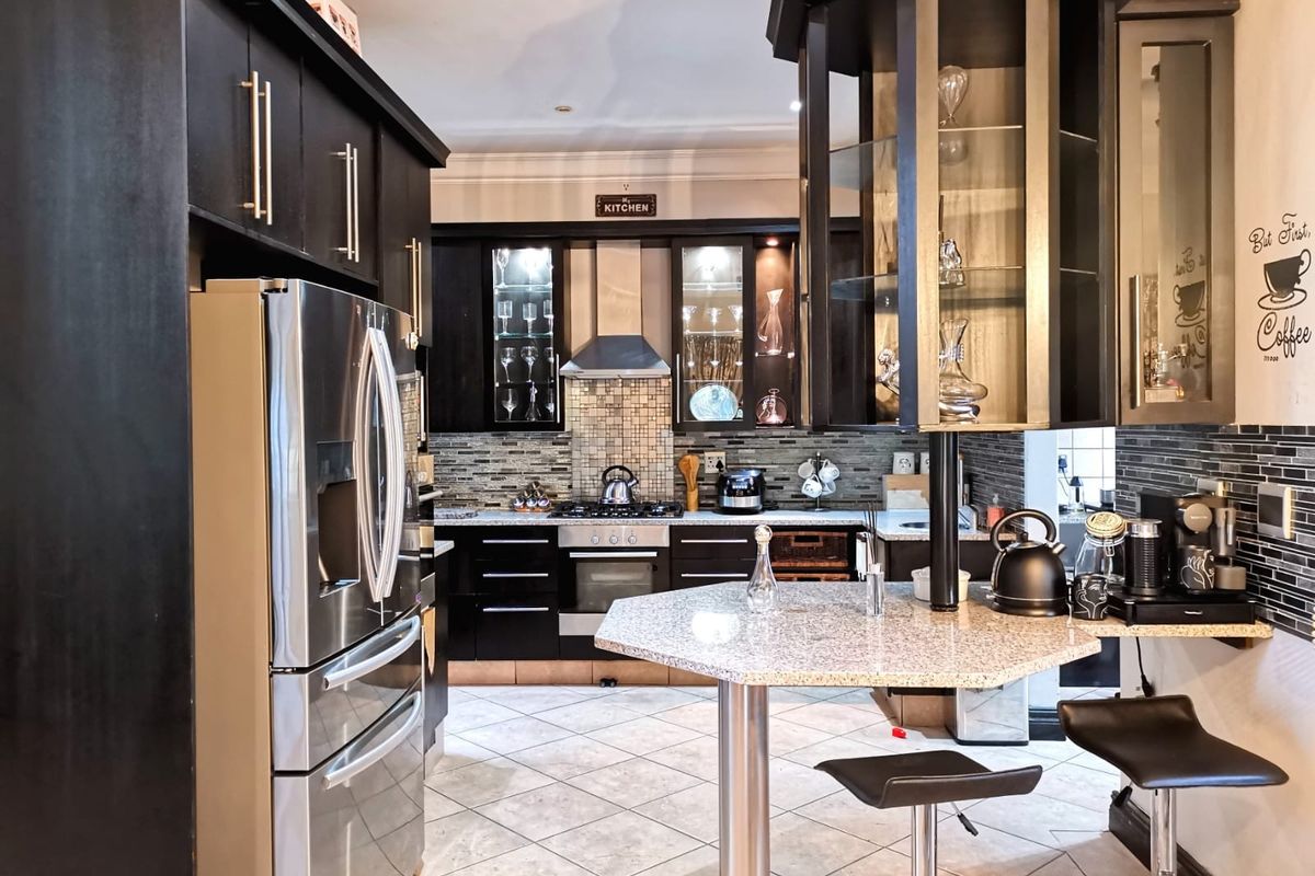 Modern kitchen featuring dark cabinetry, granite countertops, a central breakfast bar, stainless steel appliances, and a tiled backsplash.