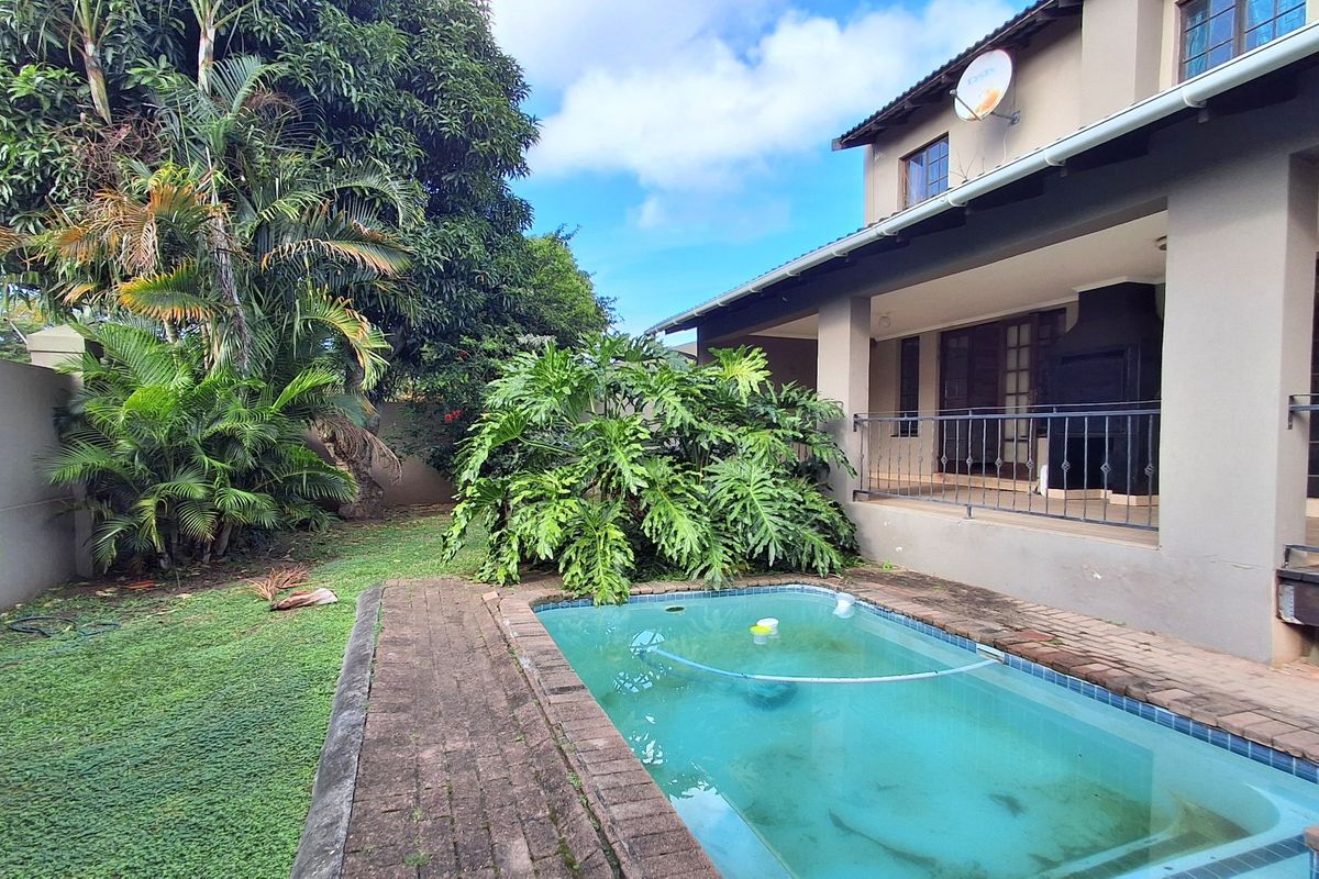 Rear view of the townhouse featuring a covered patio with built-in braai, a swimming pool, and a private garden area.