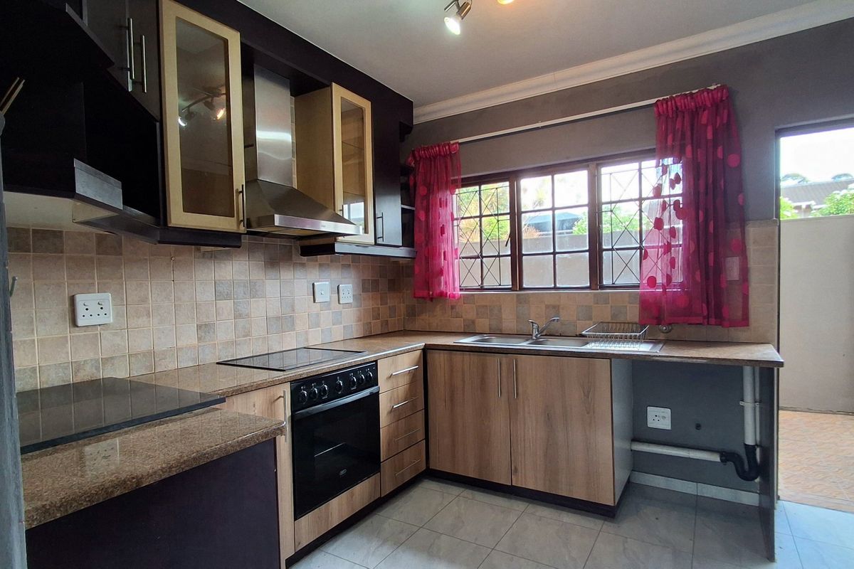 Functional kitchen featuring wood-look cabinetry, tiled backsplash, built-in oven with extractor fan, and a double sink overlooking the exterior area.