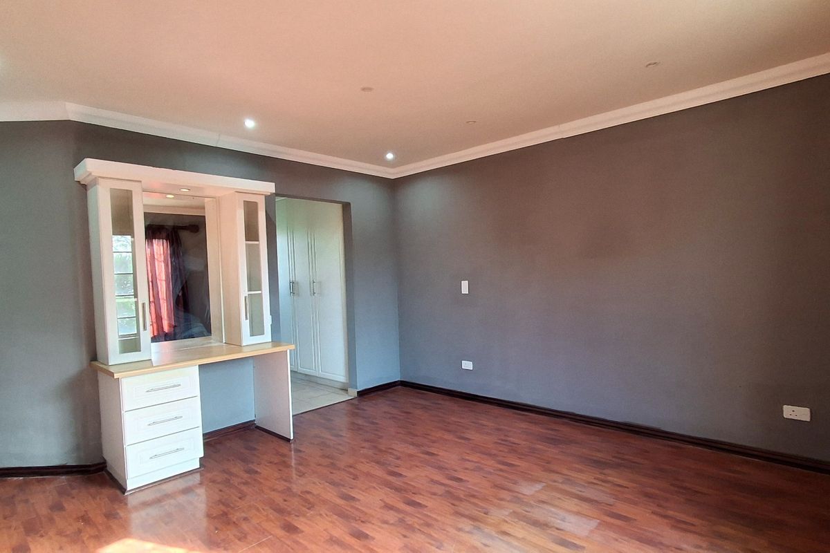 Spacious bedroom featuring dark grey walls, warm-toned laminate flooring, recessed ceiling lighting, and a built-in vanity unit with integrated storage.