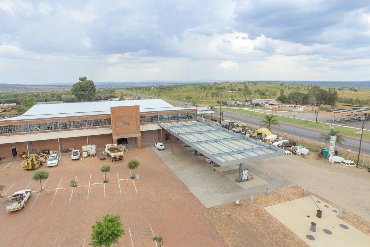Aerial view of a commercial property featuring a large warehouse building, paved parking area, and a fuel station canopy with pump infrastructure.