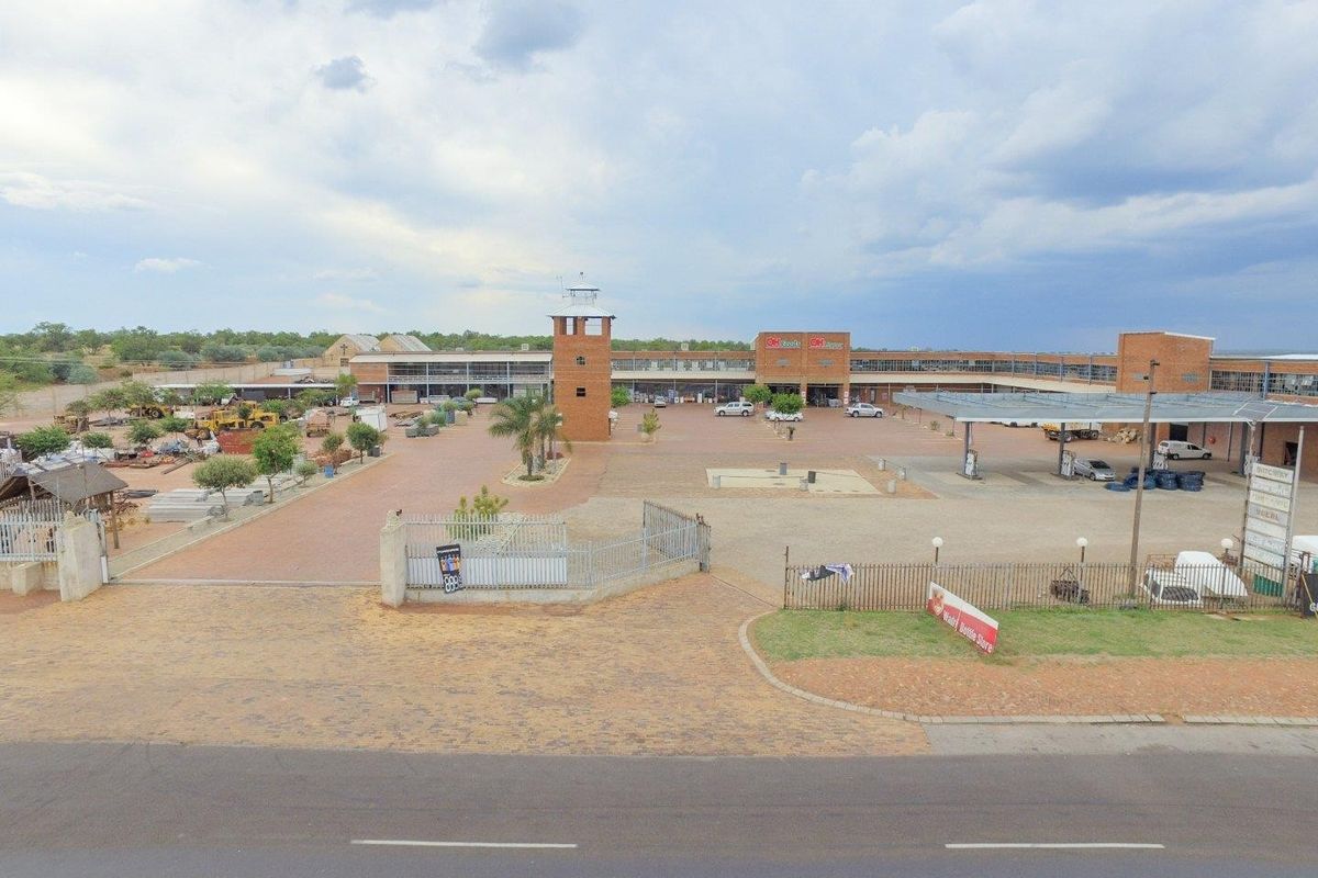 Aerial view of a commercial retail complex featuring a central courtyard, brick architecture, a fuel station canopy, and paved parking areas.