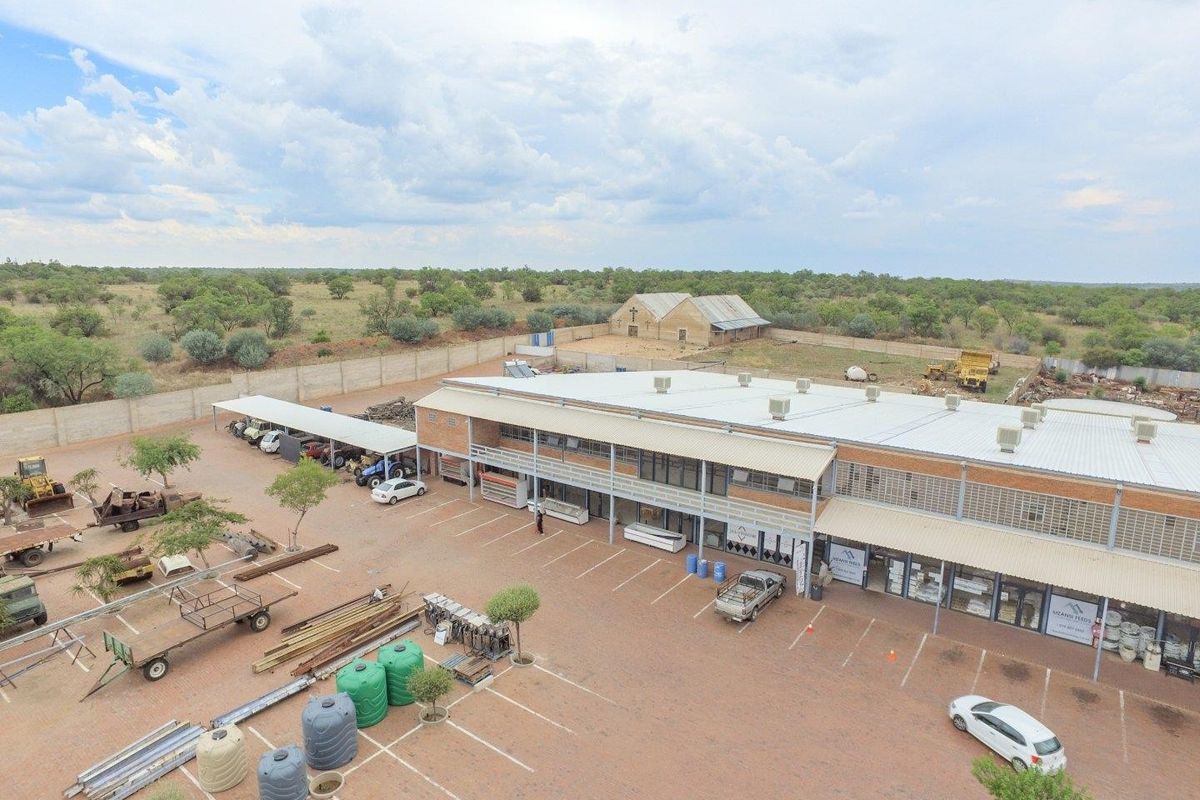 Aerial view of a commercial property featuring a large paved parking area, covered parking bays, and a multi-unit industrial or retail building.