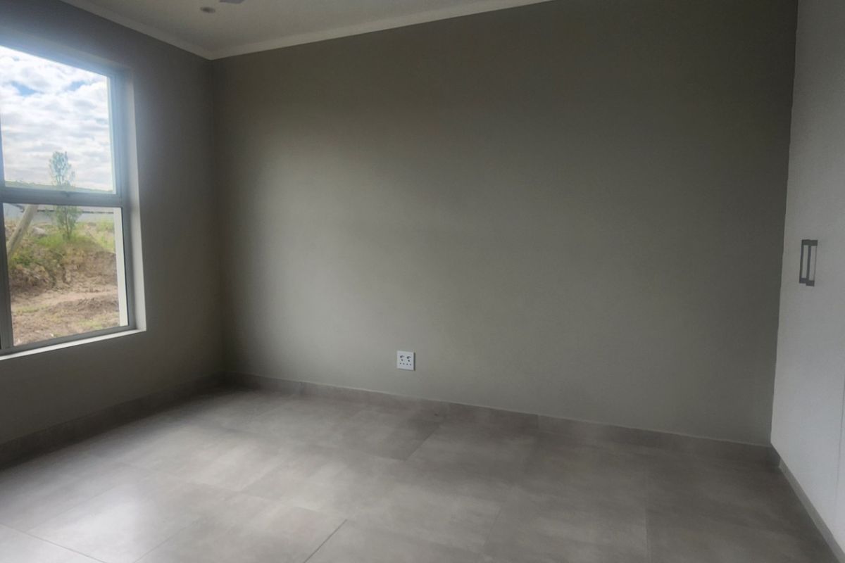 A bright, empty bedroom featuring neutral-toned walls, large windows, tiled flooring, and built-in white cabinetry.
