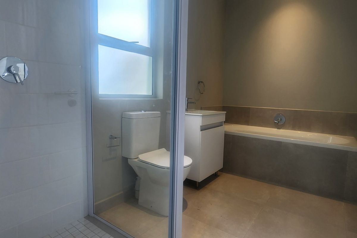 Modern bathroom featuring a glass-enclosed shower, a built-in bathtub with tiled surround, a vanity cabinet, and a toilet.