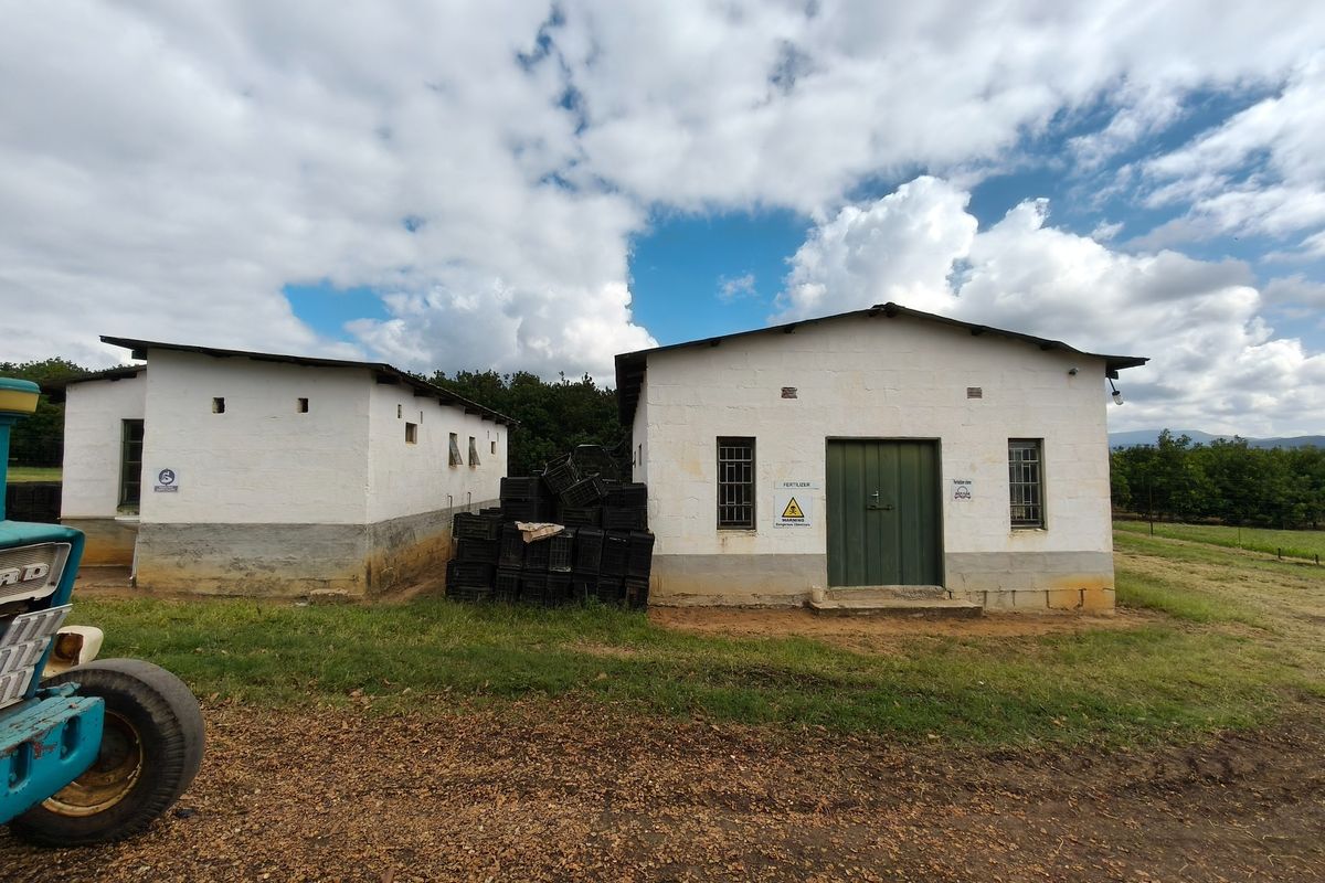 Exterior view of two functional farm outbuildings with white masonry walls, metal roofing, and secure access doors, situated on a rural property.