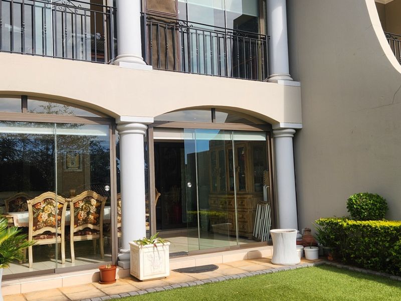 Covered ground floor patio featuring glass stacker doors, tiled flooring, and decorative columns, with an upper-level balcony above.