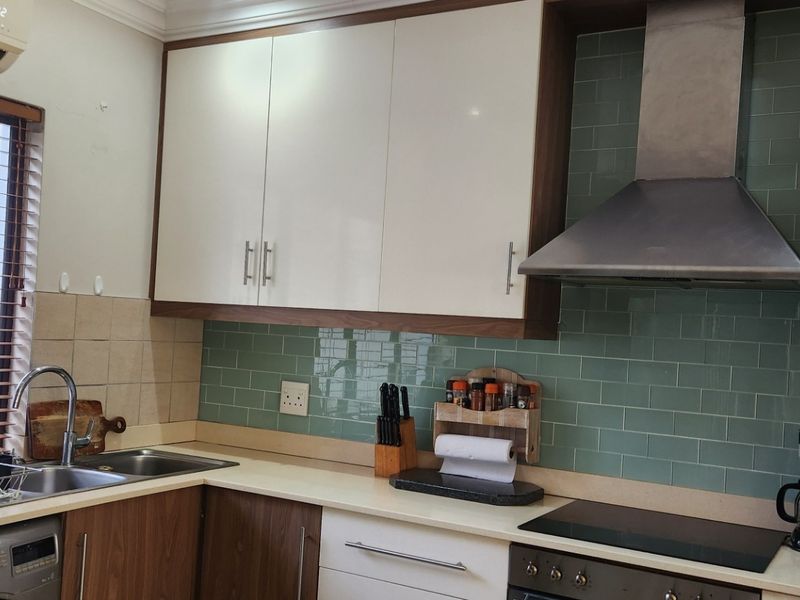 A functional kitchen featuring modern white and wood-tone cabinetry, a green subway tile backsplash, stainless steel extractor fan, and integrated cooking appliances.