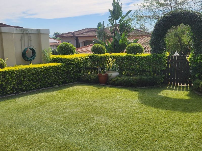 A well-maintained private garden featuring a manicured lawn, neatly trimmed hedging, and a charming wooden gate with an arched entrance.