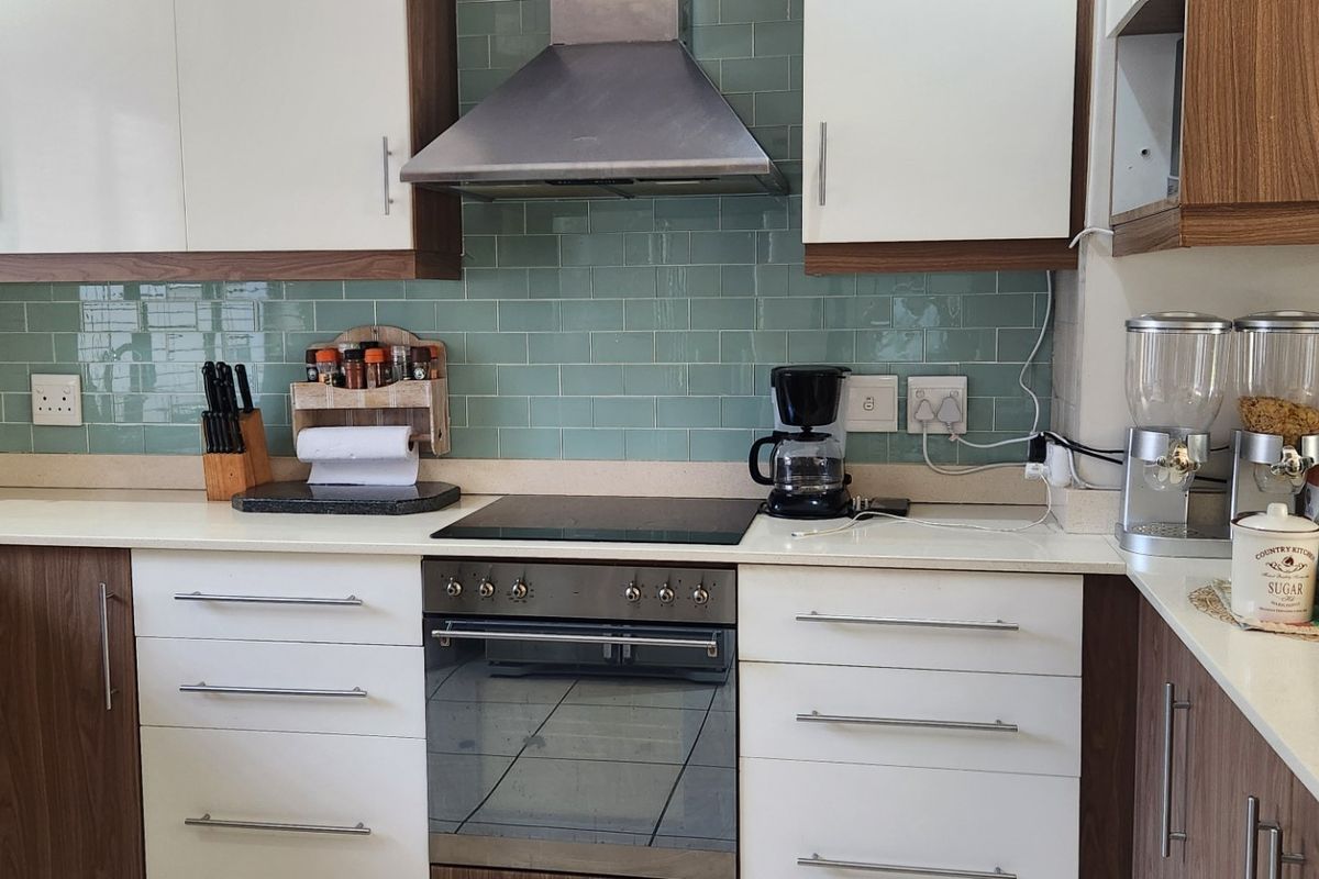 Modern kitchen featuring white and wood-tone cabinetry, a stylish green subway tile backsplash, stone countertops, and integrated stainless steel appliances.
