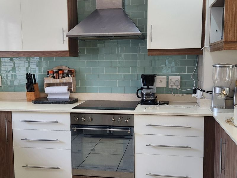 Modern kitchen featuring white and wood-tone cabinetry, a stylish green subway tile backsplash, stone countertops, and integrated stainless steel appliances.