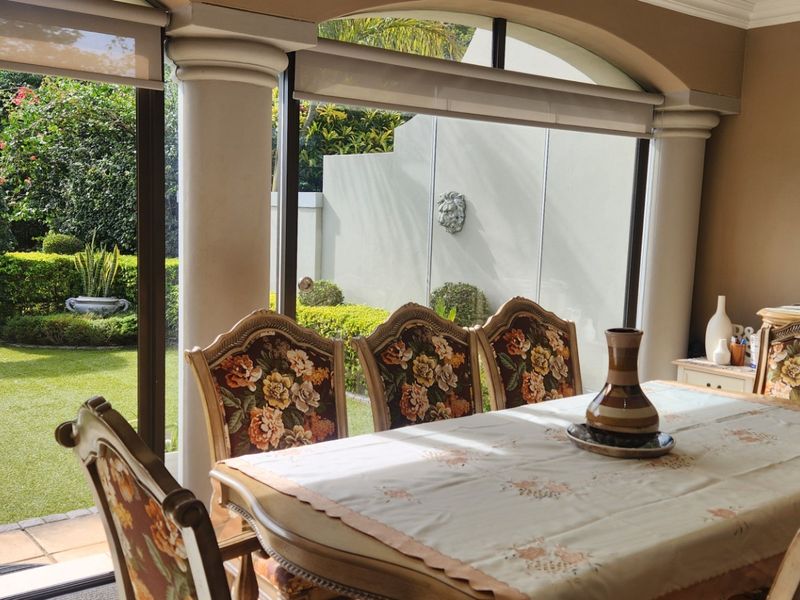 A dining room featuring large glass sliding doors that open onto a landscaped garden, complemented by architectural columns and arched window detailing.
