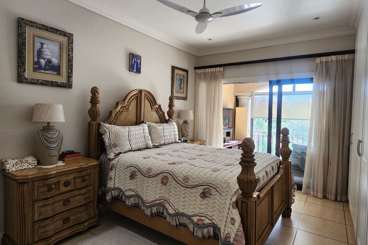 A well-maintained bedroom featuring built-in cupboards, tiled flooring, a ceiling fan, and a sliding glass door providing access to an outdoor area.