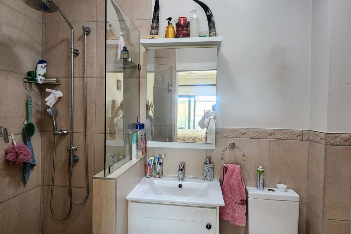 A functional bathroom featuring a walk-in shower with glass screen, vanity cabinet with basin, and a standard toilet, finished with neutral wall tiling.