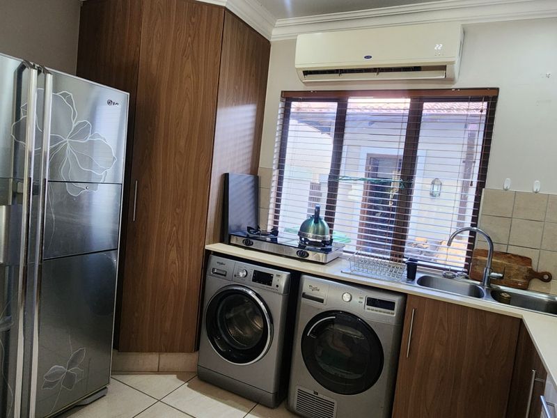 A functional laundry area featuring built-in wooden cabinetry, a stainless steel sink, tiled backsplash, and space for laundry appliances.