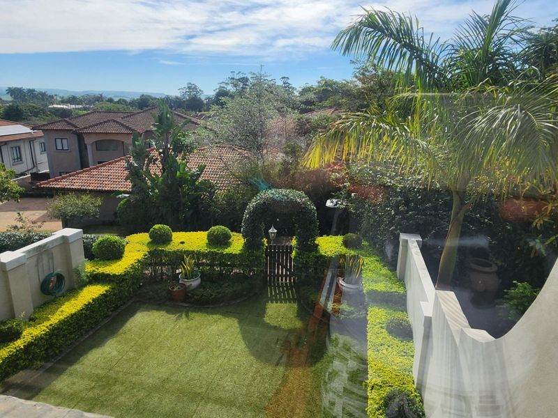Elevated view overlooking a well-maintained private garden with manicured hedges, a central archway, and surrounding residential estate landscape.