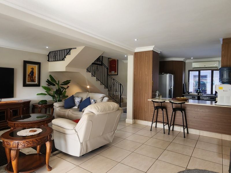 Spacious open-plan living area featuring a kitchen with breakfast bar, tiled flooring, and a staircase with decorative wrought iron balustrade.