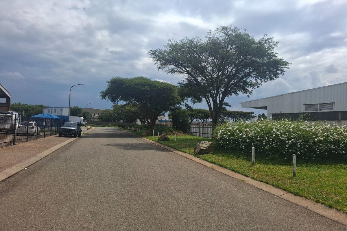 A view of the industrial property street frontage featuring paved access roads, landscaped verges, and perimeter security fencing.