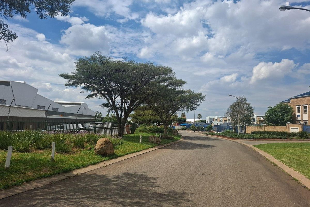 A view of the paved access road and landscaped verge within the industrial park, featuring established trees and perimeter security fencing.